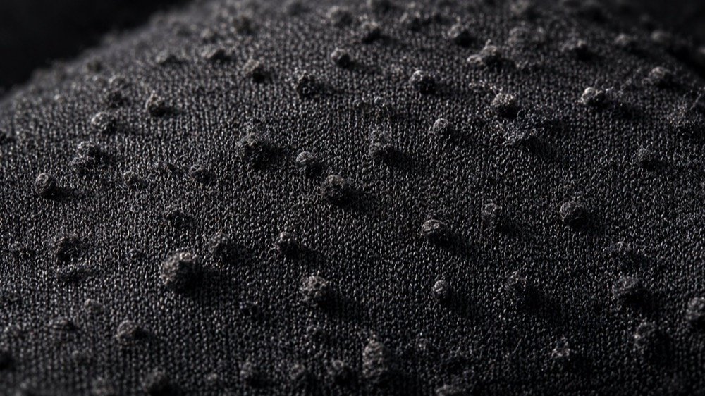 Close-up of pilling balls on black activewear fabric surface after wear and abrasion