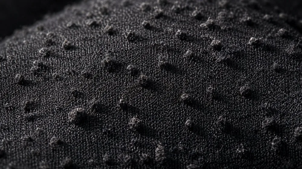 Close-up of pilling balls on black activewear fabric surface after wear and abrasion